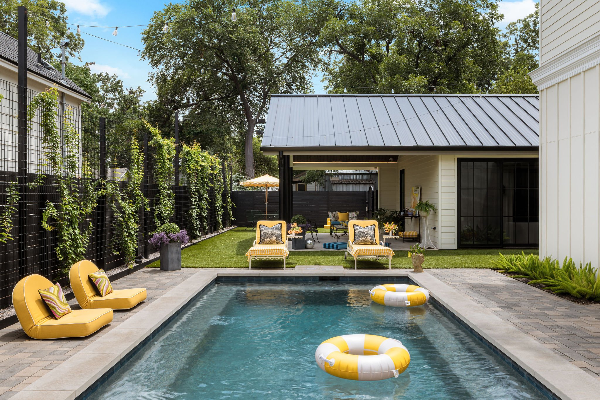 Pool with yellow floats and loungers leading to a metal-roof cabana under string lights