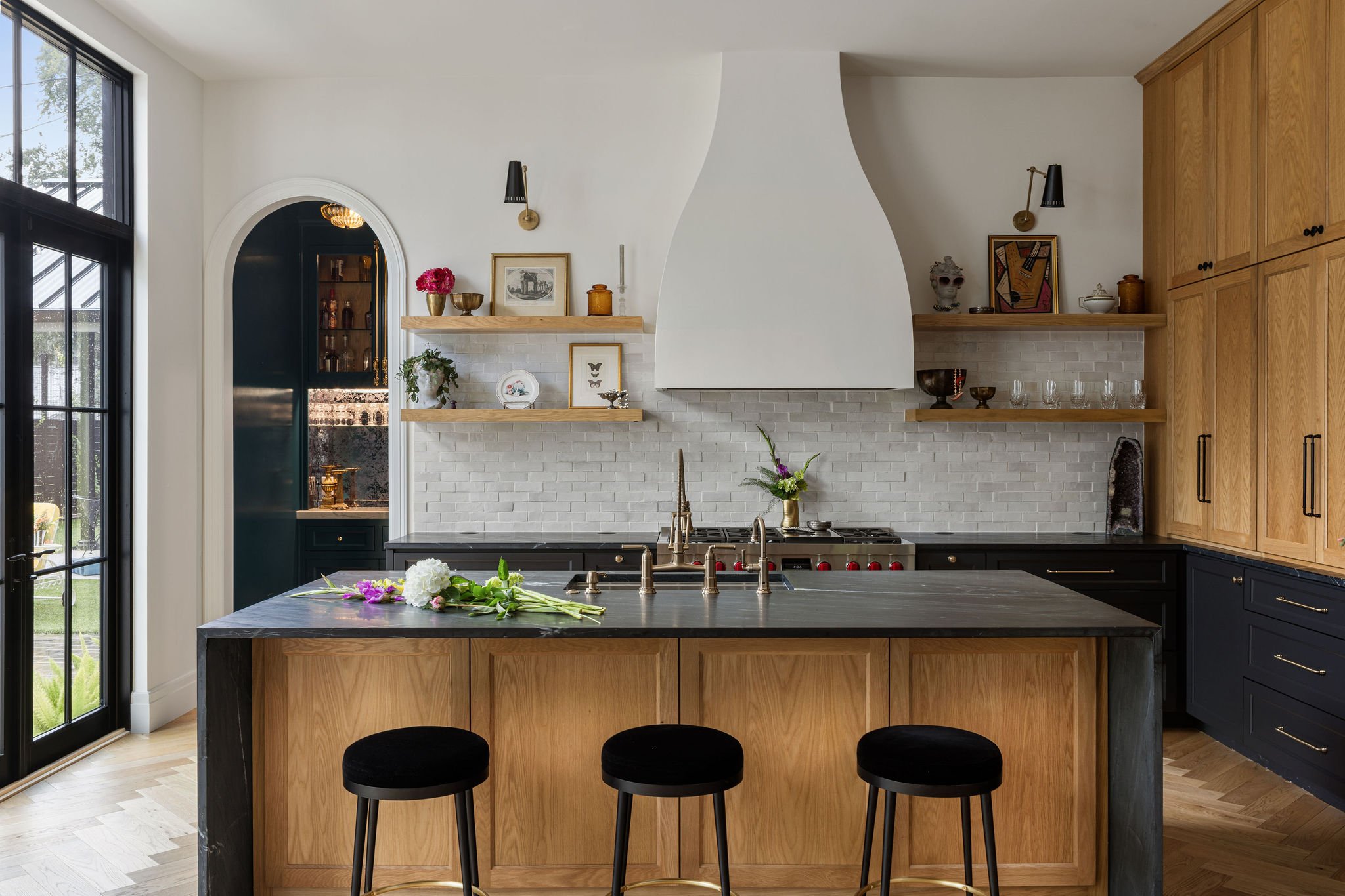 Kitchen with oak island, three black stools, plaster range hood, and open wood shelves