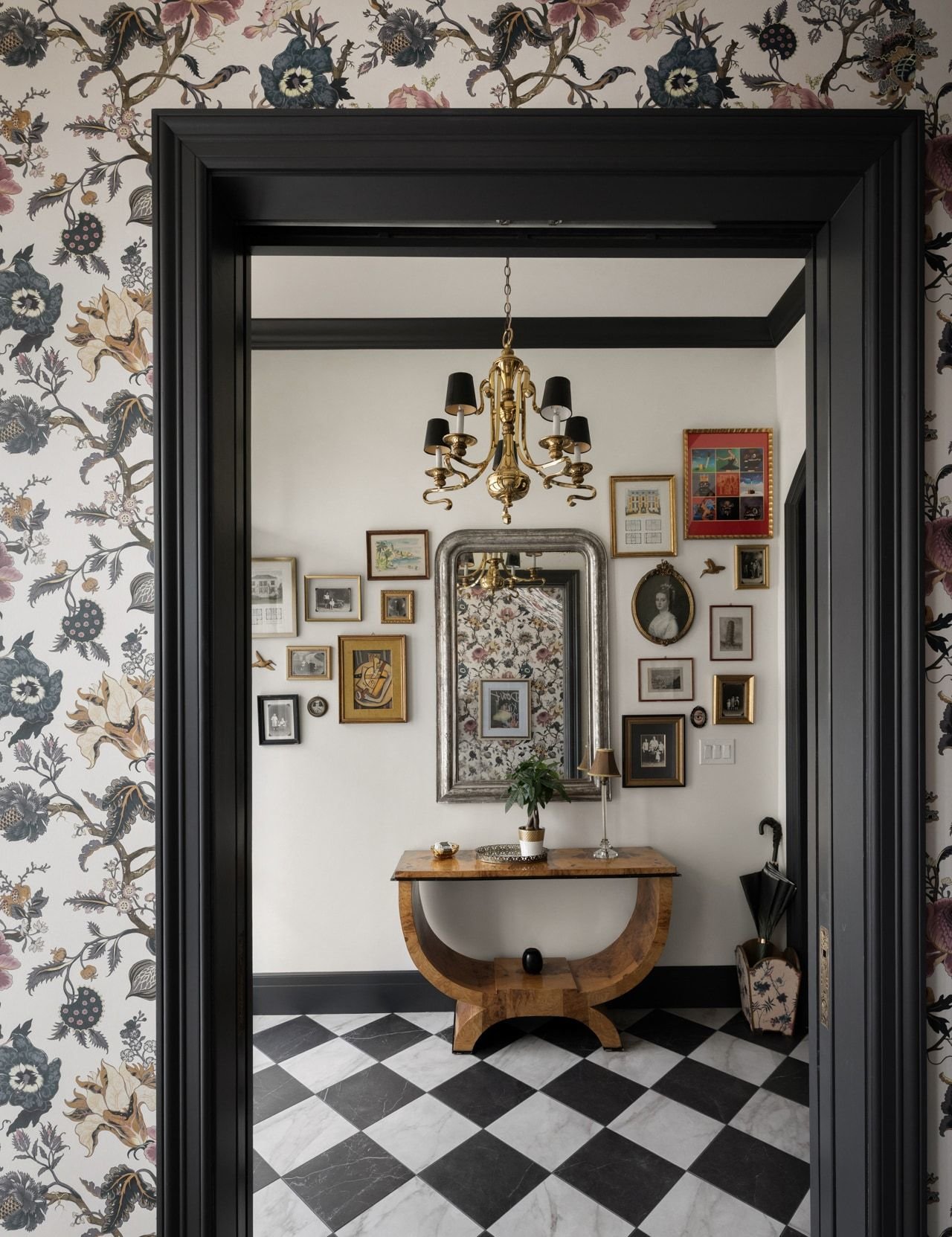 View through a black doorway framed by floral wallpaper into an entry with checkered floor, chandelier, and gallery wall