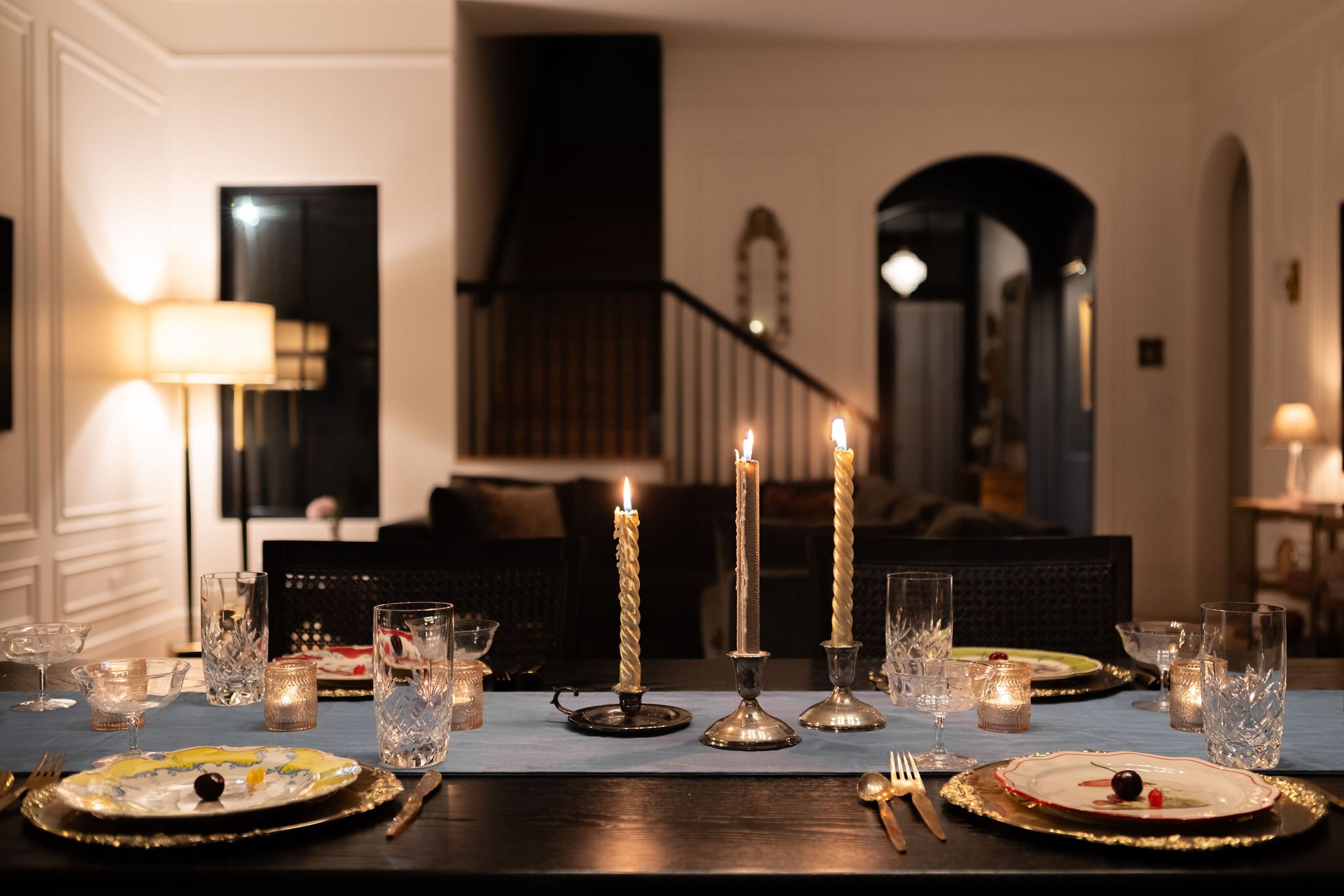 Candlelit dinner table in the foreground with the living room, staircase, and arched doorway beyond