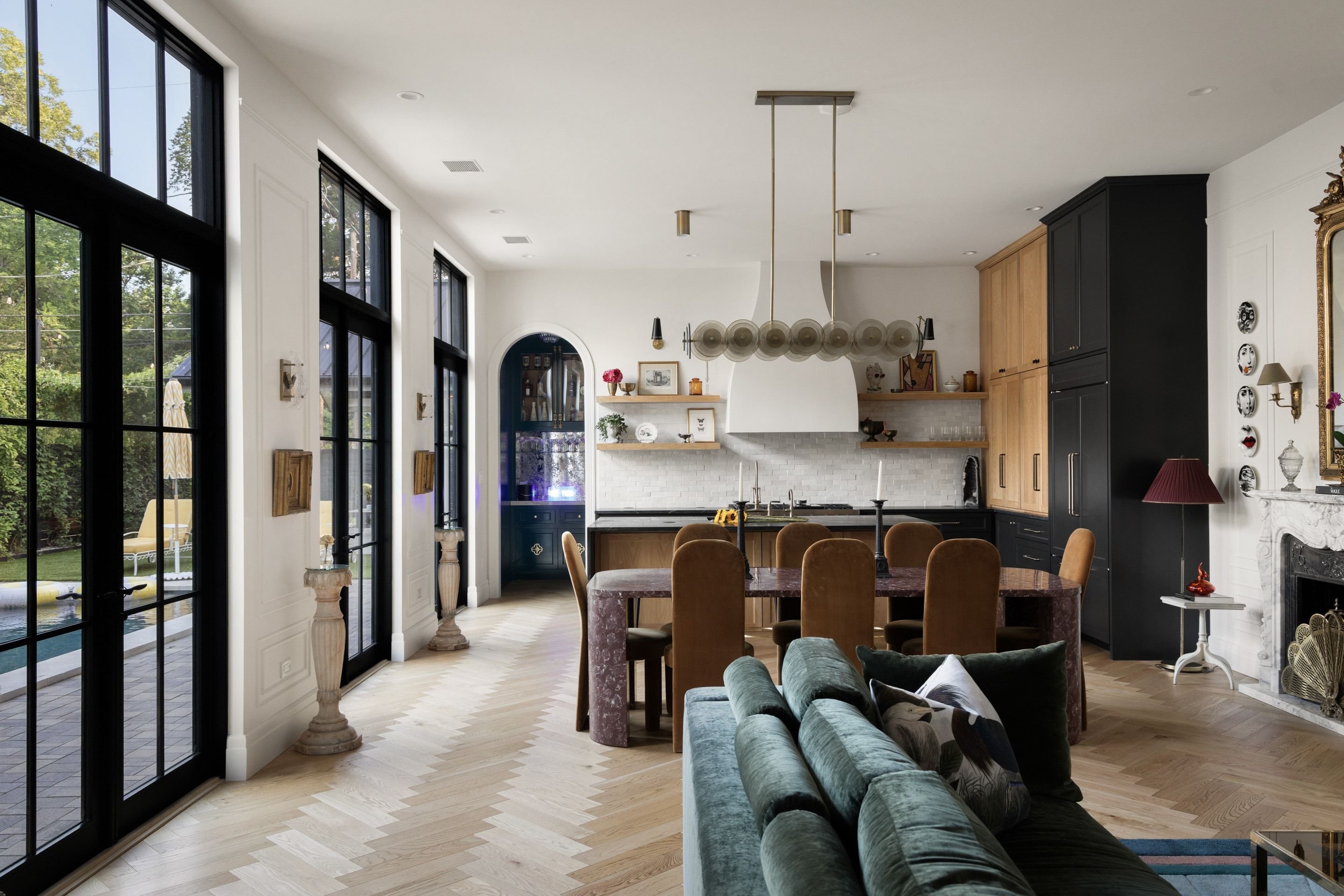 Open-plan kitchen and dining room with black steel windows, herringbone oak floors, a long dining table, and a green velvet sofa